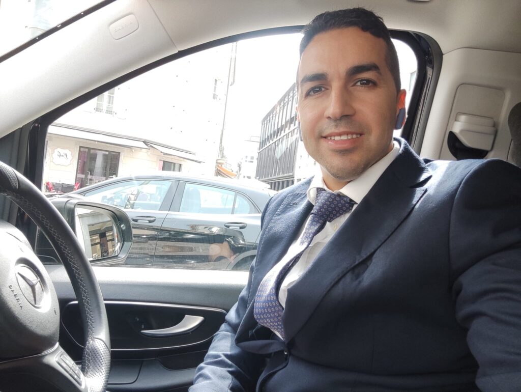 Professional chauffeur standing beside a black Mercedes van with panoramic Lake Como view, offering premium private transfer services.